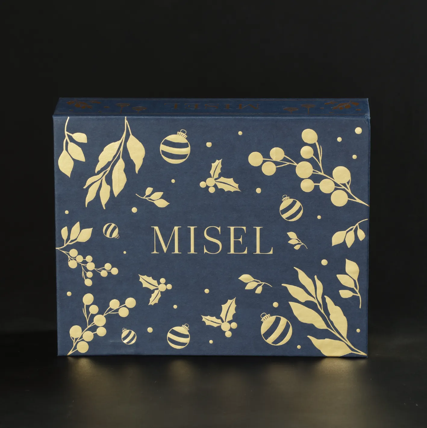 合上嘅深藍色 MISEL 書型禮盒,Logo 周圍燙金冬青、漿果同聖誕球
